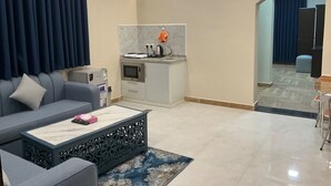 A modern living room with a grey sofa, a coffee table, and a kitchen area with a microwave and kettle. - AlBaidaa AlSalam branch (Madinah)