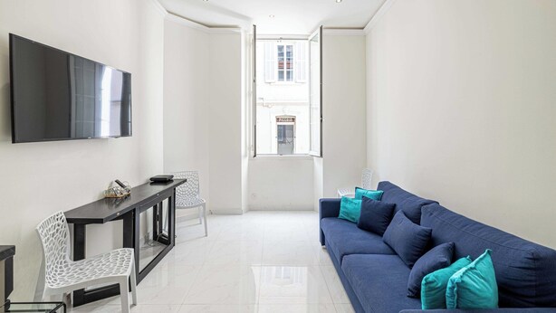 A modern living room with a flat-screen TV, a blue sofa with teal cushions, a white chair, and a small table with a tray. - Beautiful Two bedroom apartment near Croisette (Cannes)