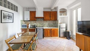 Een moderne keuken met houten kastjes, een eettafel met gestoffeerde stoelen, een ingebouwde oven en een grote televisie.