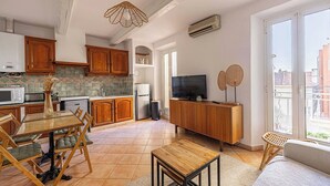 Een moderne keuken met houten kastjes, een eettafel met stoelen, een televisie en een balkon met rieten meubilair.