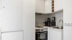 A compact kitchen with white cabinetry, a built-in oven, a coffee maker, and a sink.