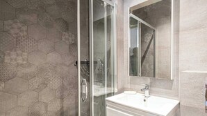 A modern bathroom with a glass shower enclosure, a white sink, and a large mirror.