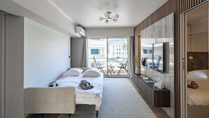 A modern hotel room with a bed, a desk, a TV, and a balcony with a view of buildings.