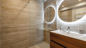 A modern bathroom with a marble wall, a glass-enclosed shower, and a vanity with a mirror.