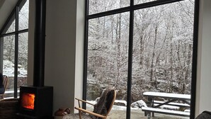 A cozy room with a large window, a fireplace, a chair, and a view of a snowy forest.