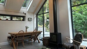 A modern interior with a dining area, large windows, and a wood-burning stove.