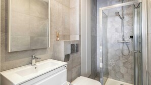 Et moderne badeværelse med et stort spejl, en hvid vask, et toilet og et bruseområde med glasvægge.