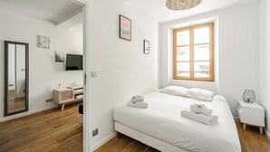 Et moderne hotelværelse med en stor seng, et fjernsyn, trægulv og et vindue med naturligt lys.