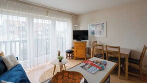 Una sala de estar con un sofá, una mesa de centro, un televisor sobre un mueble de madera y un comedor con sillas.