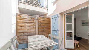 Un petit pati exterior amb una taula i cadires de fusta, una porta amb persianes blava i un balcó amb barana metàl·lica.