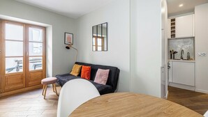 Un saló modern amb un sofà, taula de dinar i zona de cuina visible a través d'una porta oberta.
