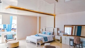 A modern hotel room with a large bed, a sitting area with a sofa and ottoman, a desk with a chair, and a large window offering a view. - Recidencia Del Hamor Beachfront (Santa Magdalena)