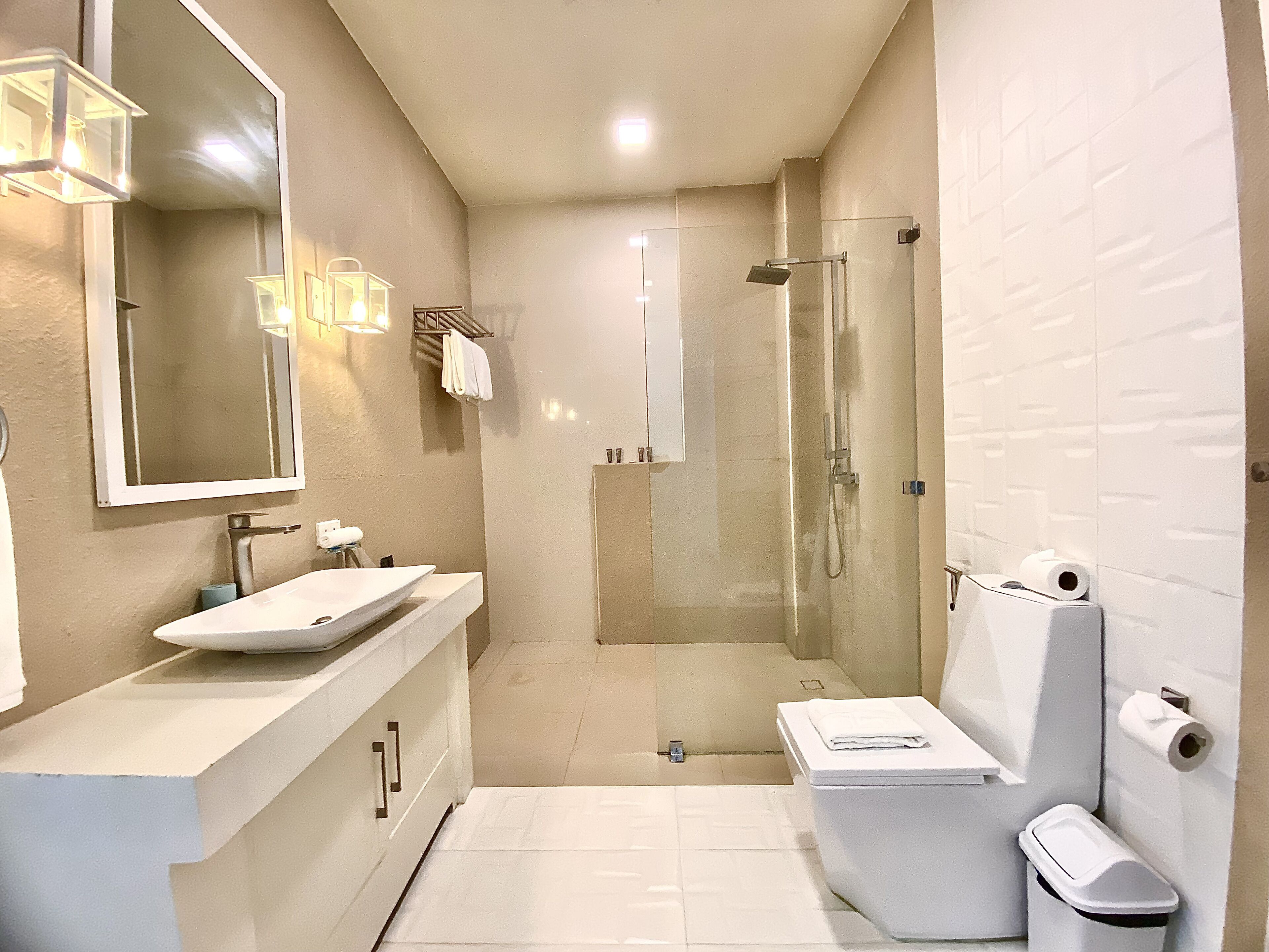 Un baño moderno con un espejo grande, un lavamanos, un inodoro y una ducha con mampara de vidrio.