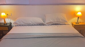 Una cama bien hecha con una colcha estampada, dos lámparas de noche y un pequeño banco frente a la cama.