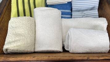 Een houten dienblad met netjes gevouwen handdoeken in verschillende kleuren en patronen, waaronder wit, groen en blauw, op een betegelde vloer.