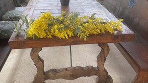 Una mesa de madera con un jarrón de flores amarillas y un banco con cojín.