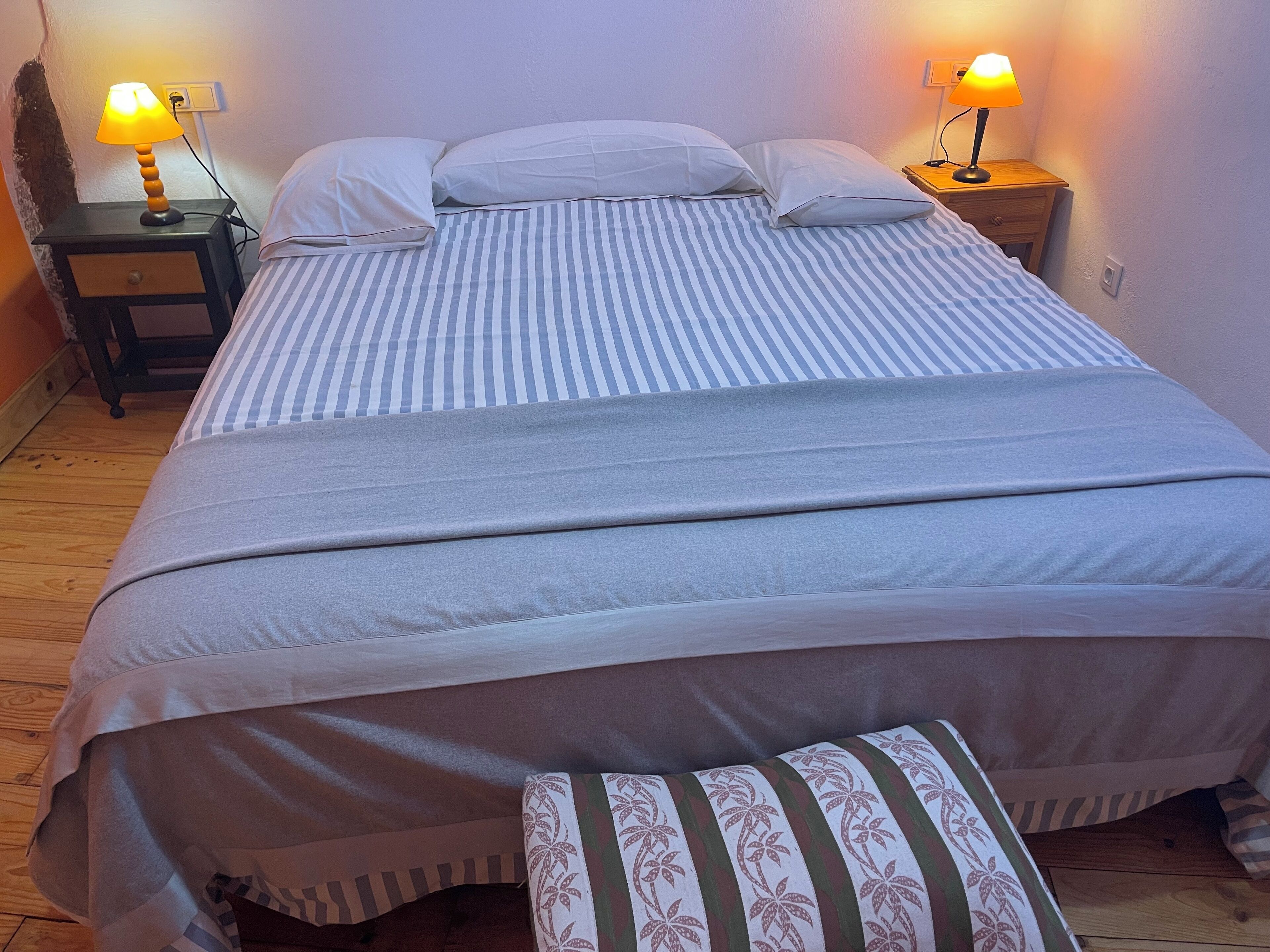 A neatly made bed with striped bedding, two bedside lamps, and a wooden nightstand.