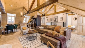 A spacious loft-style living area with high ceilings and exposed wooden beams, a cozy seating arrangement, and a kitchen in the background. - Gorgeous 3 Bedroom 2-floor Old Townhouse (Québec)