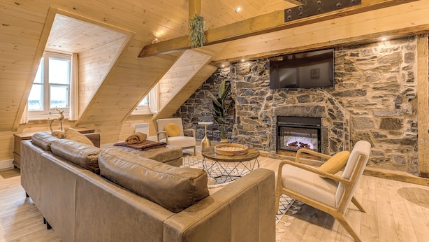 A cozy loft-style living room with a stone fireplace, wooden beams, and a large window. - Gorgeous 3 Bedroom 2-floor Old Townhouse (Québec)