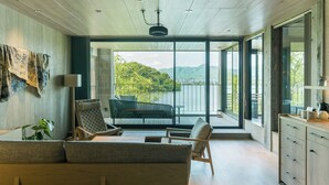A modern living room with a sofa, chairs, and a dining table. There is a large window with a view of a mountain and greenery. - HOTEL and KOTEI SOKA (Kyotango)