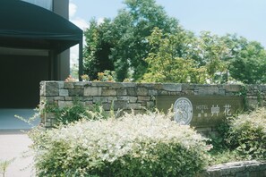 A stone wall with a hotel sign, surrounded by greenery and trees. - HOTEL and KOTEI SOKA (Kyotango)