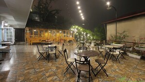 An outdoor patio area with stone flooring, wooden tables and chairs, and string lights. - SaPa Signature Inn (Sa Pa)