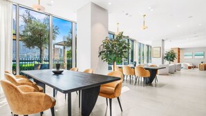 Un moderno vestíbulo de hotel con una gran mesa de comedor, asientos cómodos, ventanas amplias con vistas a la ciudad y plantas de interior.