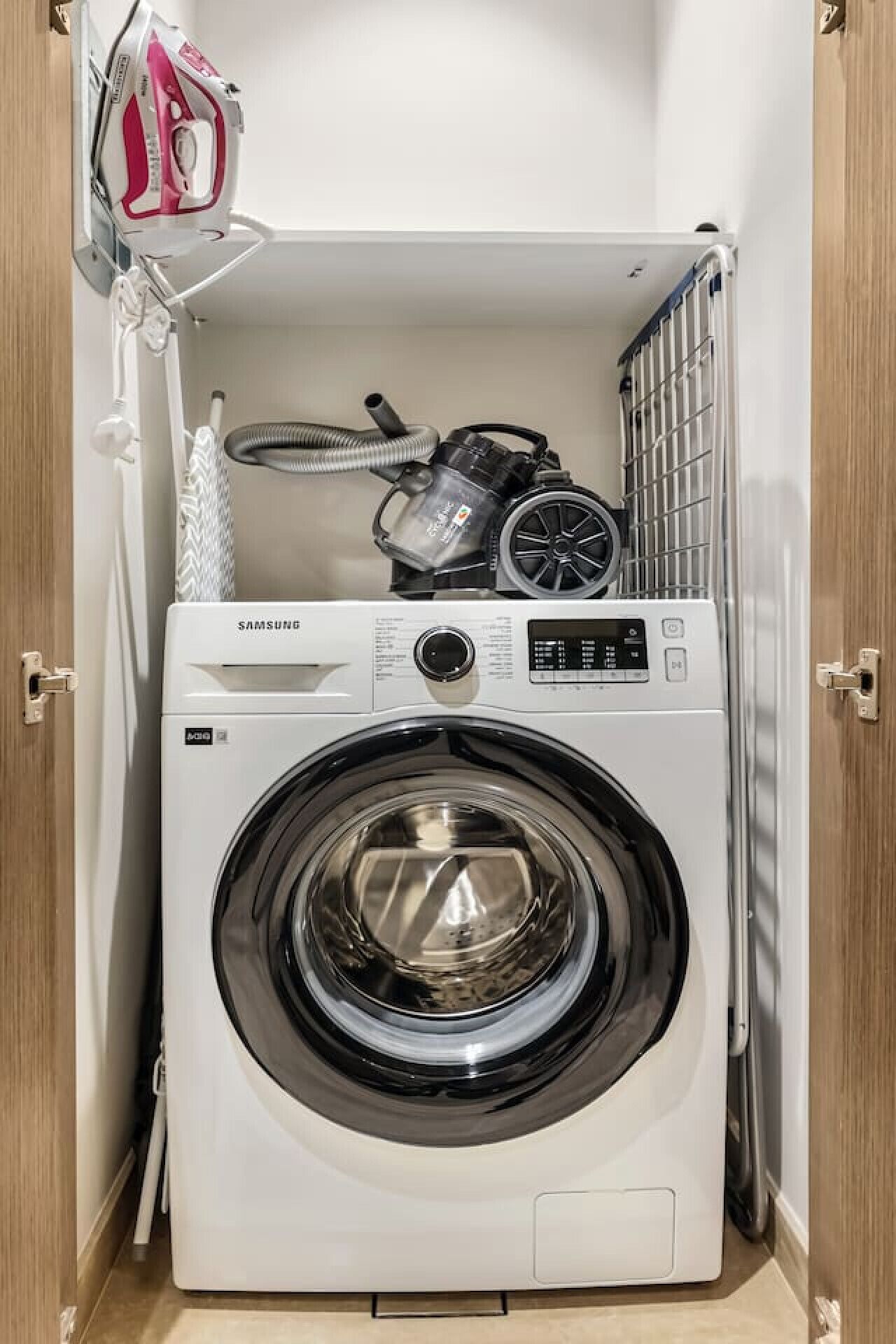 Une machine à laver Samsung dans une buanderie, avec un étendoir et un fer à repasser.