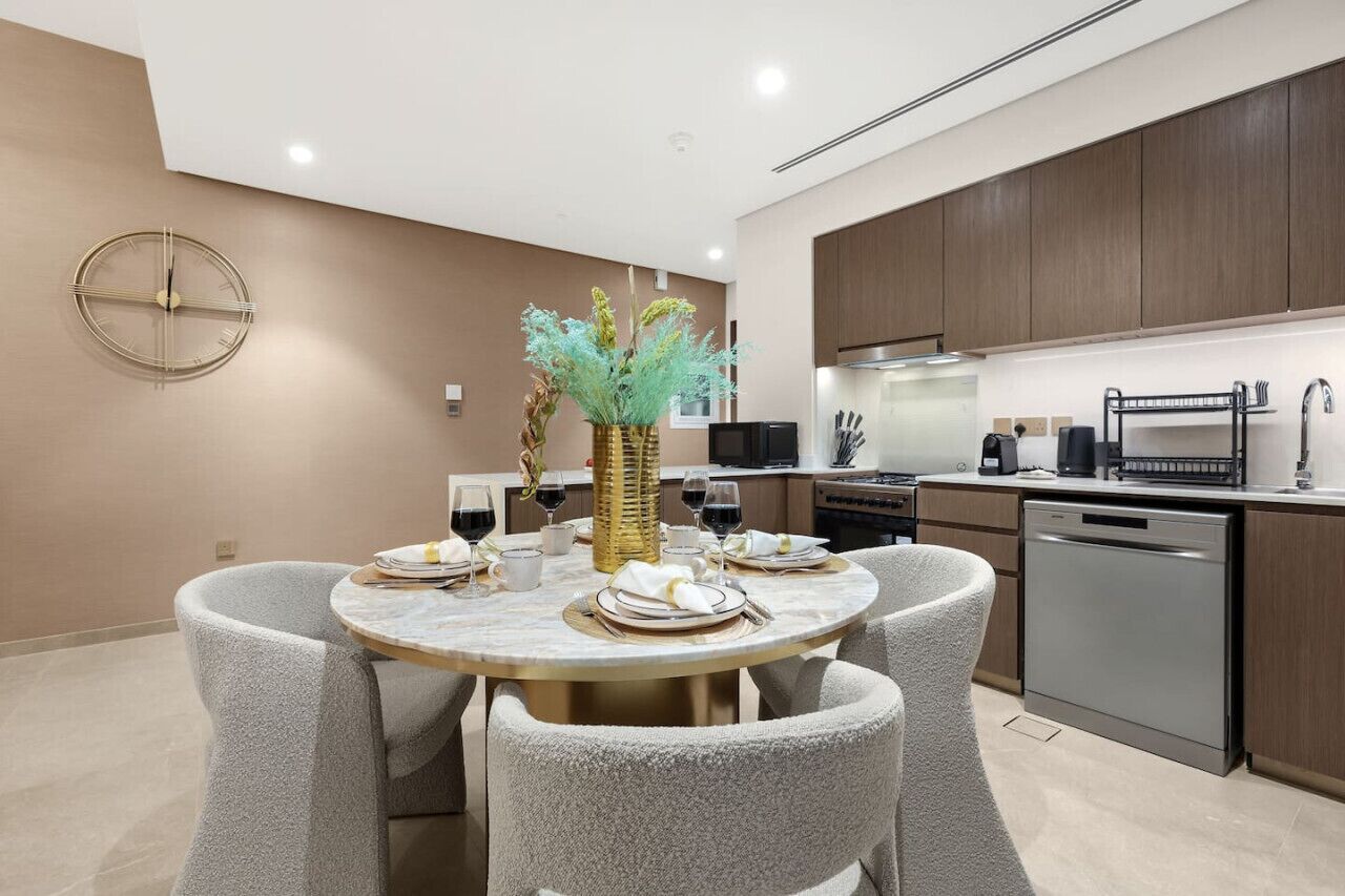 Una cocina moderna con armarios de madera oscura, lavavajillas de acero inoxidable y una mesa de comedor redonda con sillas tapizadas en gris.