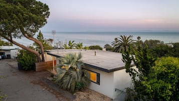 Una casa moderna con techo plano, un árbol grande y vista al mar.