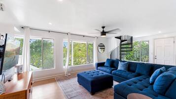A modern living room with a large sectional sofa, a flat-screen TV, and a staircase leading to an upper level.