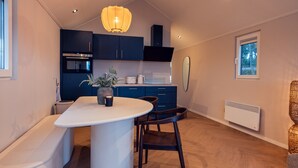 Une cuisine moderne avec des meubles de couleur bleu foncé, un plan de travail blanc et un îlot central. On y trouve un four et un micro-ondes encastrés, un luminaire suspendu et une fenêtre donnant sur les arbres.