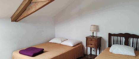 A bedroom with two beds, wooden beams on the ceiling, a nightstand with a lamp, and a chair.