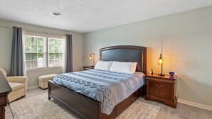 A bedroom with a bed, bedside tables, a chair, a window with curtains, and a ceiling light.