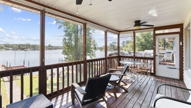 A covered deck with a view of a lake, outdoor furniture, and ceiling fans.