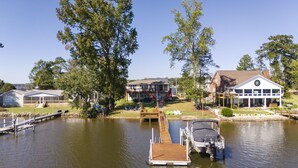 A lakeside property with a dock, a house with a large deck, and a building with a circular window.