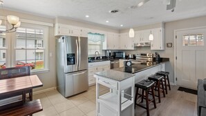 A modern kitchen with stainless steel appliances, a central island with bar stools, and a dining area with a wooden table.