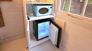 Eine kleine Küche mit eingebauter Mikrowelle und einem Mini-Kühlschrank, einem Holzregal mit Wasserkocher und einem Fenster mit Blick auf Bäume.