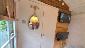 Ein Zimmer mit Holzboden, einer weißen Tür, einem Spiegel, einem Fernseher und einer kleinen Holzablage.