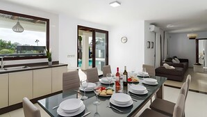 A modern dining area with a glass table, white plates, wine glasses, and a variety of fruits. - Luxury Villa with Private Pool and Stunning Views in Playa Blanca, Lanzarote (Playa Blanca)