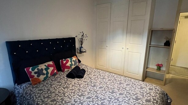 Une chambre à coucher comprenant un lit, une table de chevet, une armoire et une étagère avec un vase.