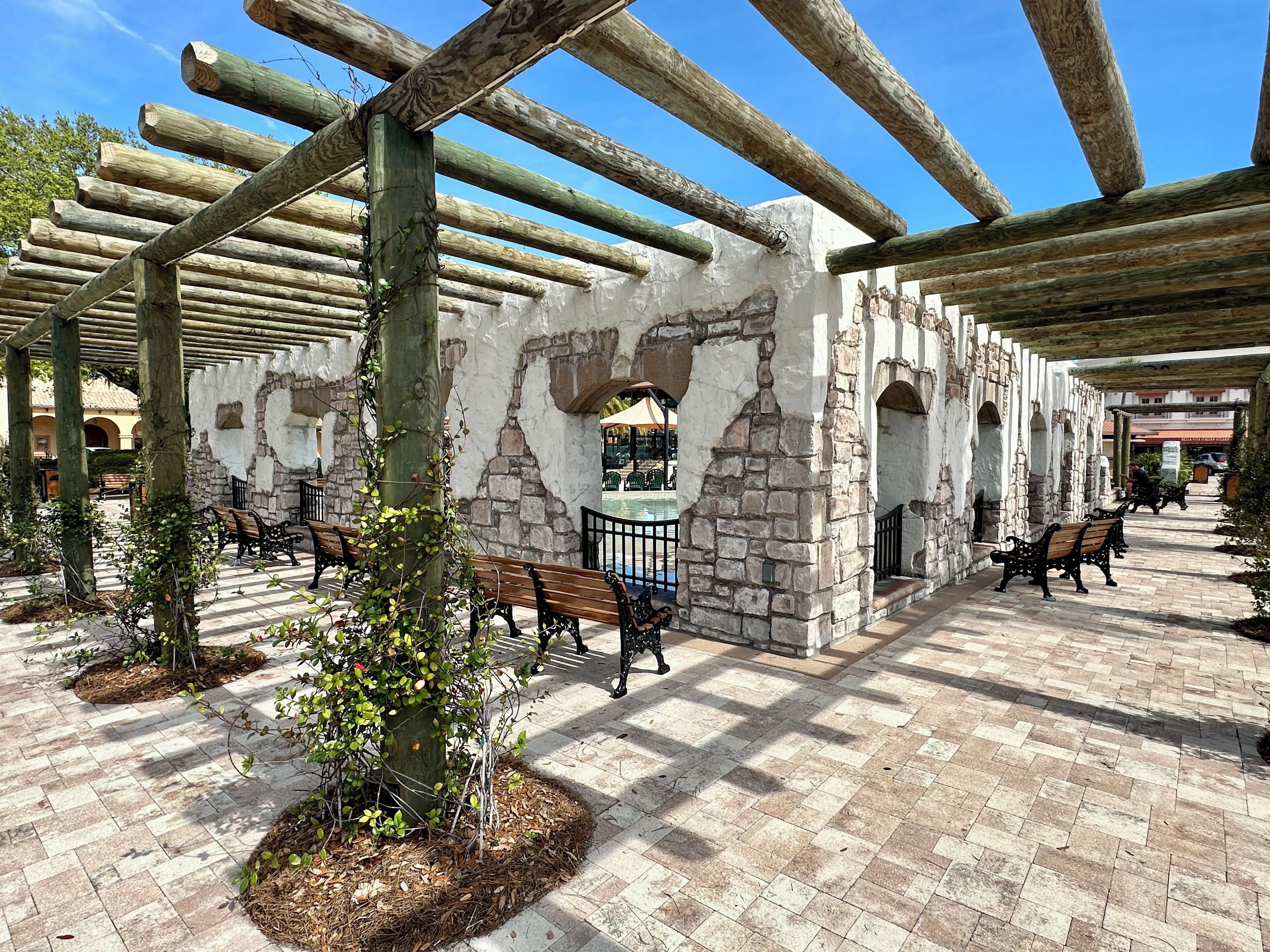A covered outdoor area with stone walls, wooden benches, and a pergola structure.