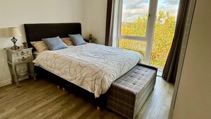 A bedroom with a large bed, a nightstand, a lamp, and a window with curtains. - Experience comfort and convenience in this ideal short-term rental! (Milton Keynes)