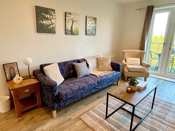 A living room with a patterned sofa, a small table, a chair, and artwork on the wall.