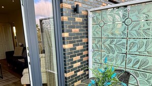 An outdoor patio with a table and chairs, a glass door leading to a room, and a decorative wall with leaf patterns. - Experience comfort and convenience in this ideal short-term rental! (Milton Keynes)