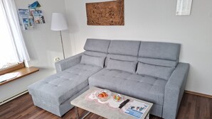 En grå hörnsoffa med ett litet soffbord framför, en lampa och en anslagstavla med broschyrer om olika resmål.