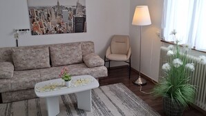 Ett vardagsrum med en soffa, ett soffbord, en lampa och en växt.
