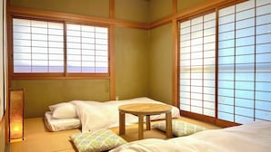 A traditional Japanese-style room with tatami flooring, two tatami mats, a low wooden table, and two beds with white bedding. - SUMITSUGU HOUSE Station (Kumamoto)