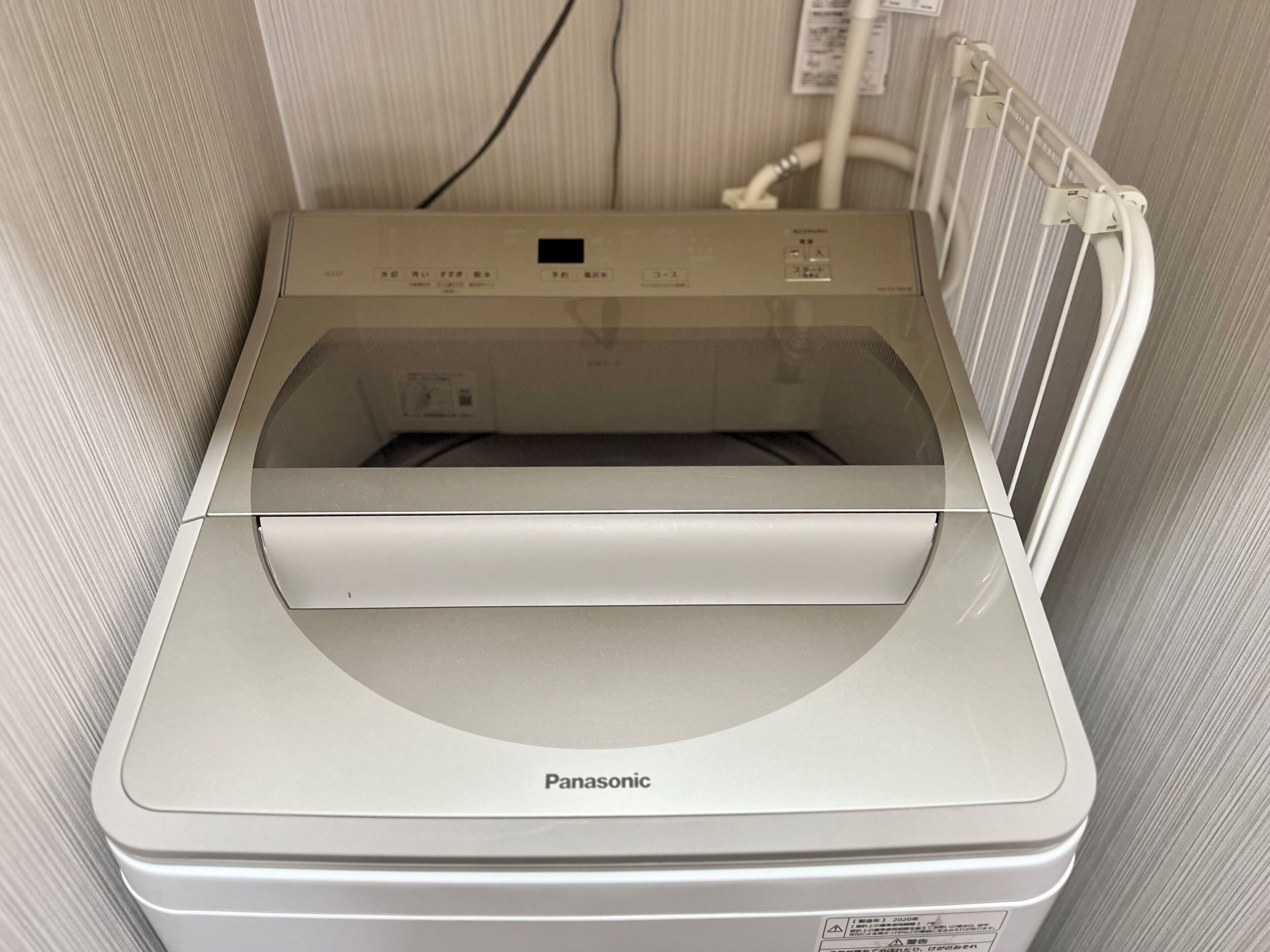 A white Panasonic washing machine in a room with striped wallpaper.