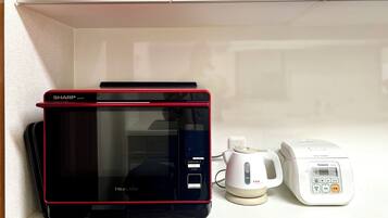 A microwave oven with a red trim, a rice cooker, and a coffee maker on a white shelf.